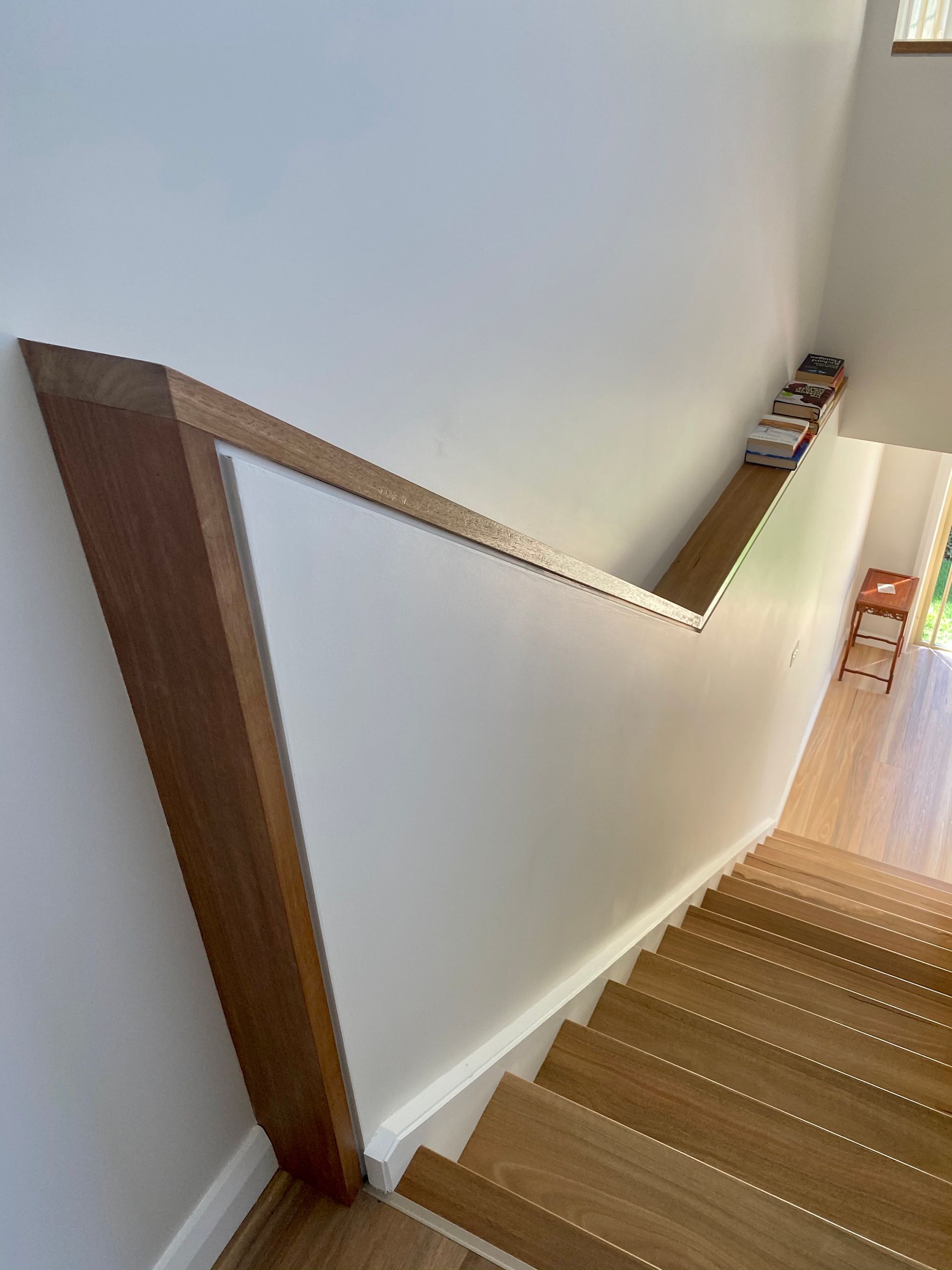 Wooden staircase with a modern handrail against a white wall.
