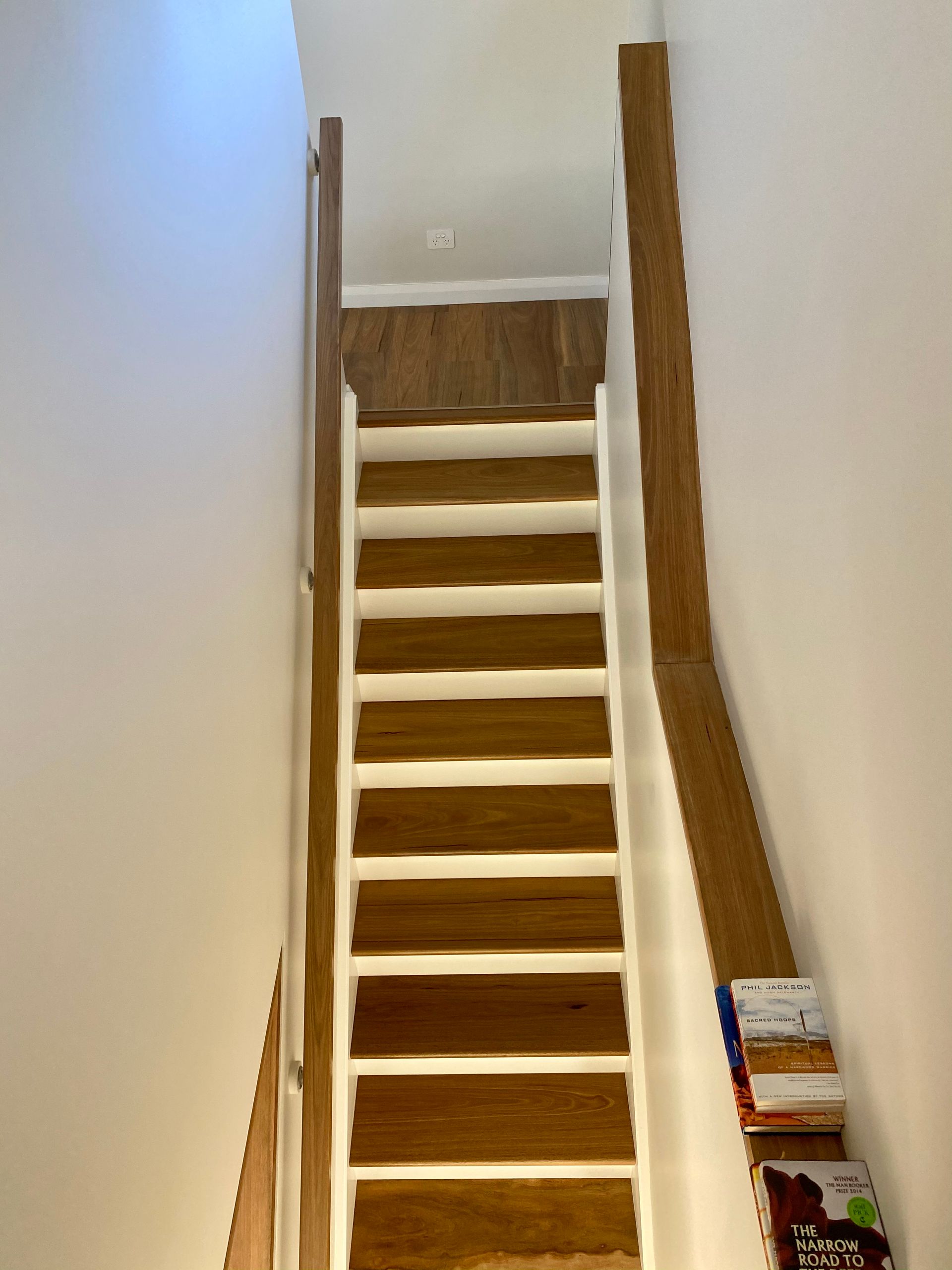 Wooden curved staircase with dark wood banister and light-colored steps. Plants in white pots are near the staircase.