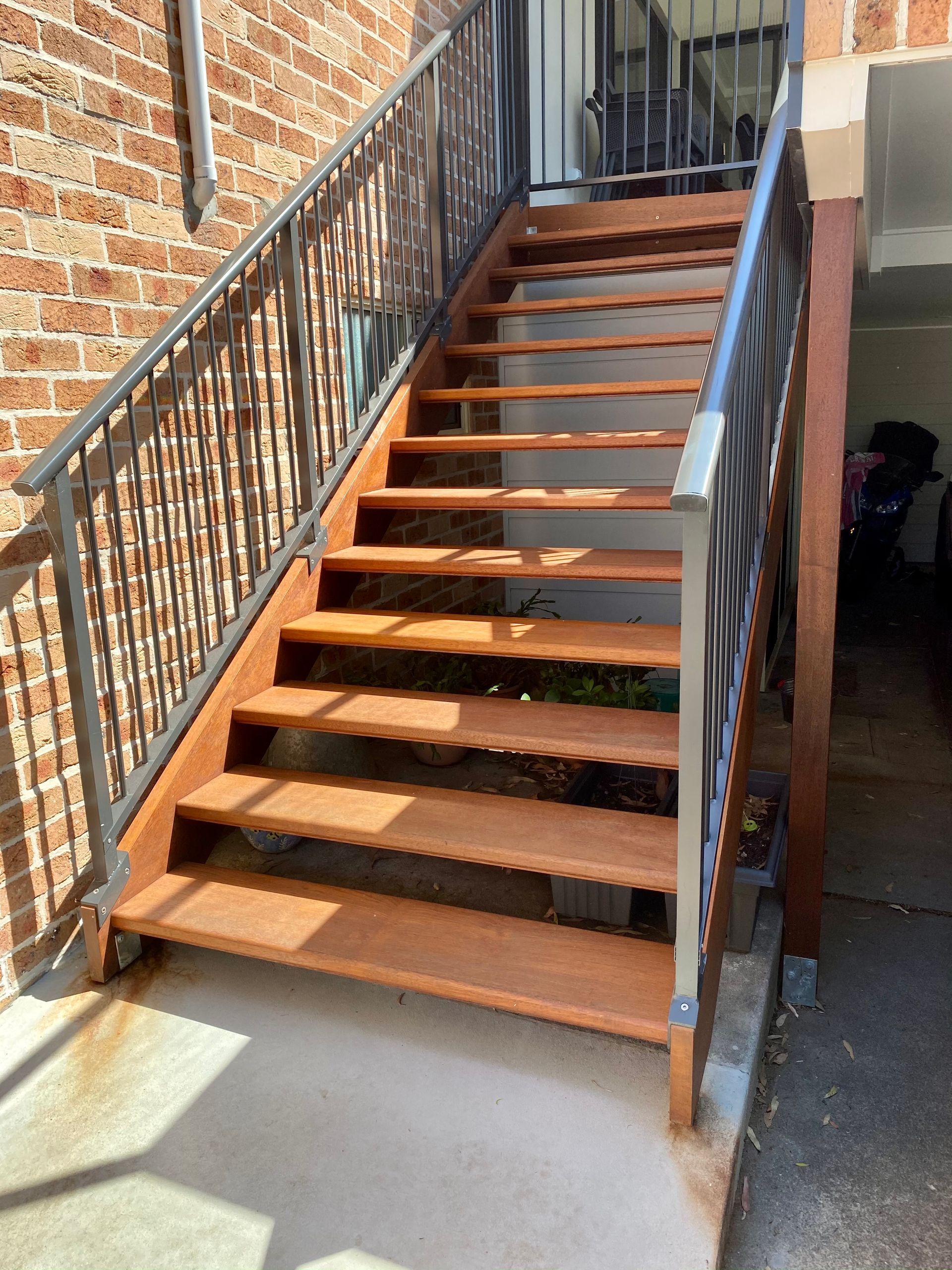 Outdoor staircase with brown wooden steps, metal railings, and brick wall.