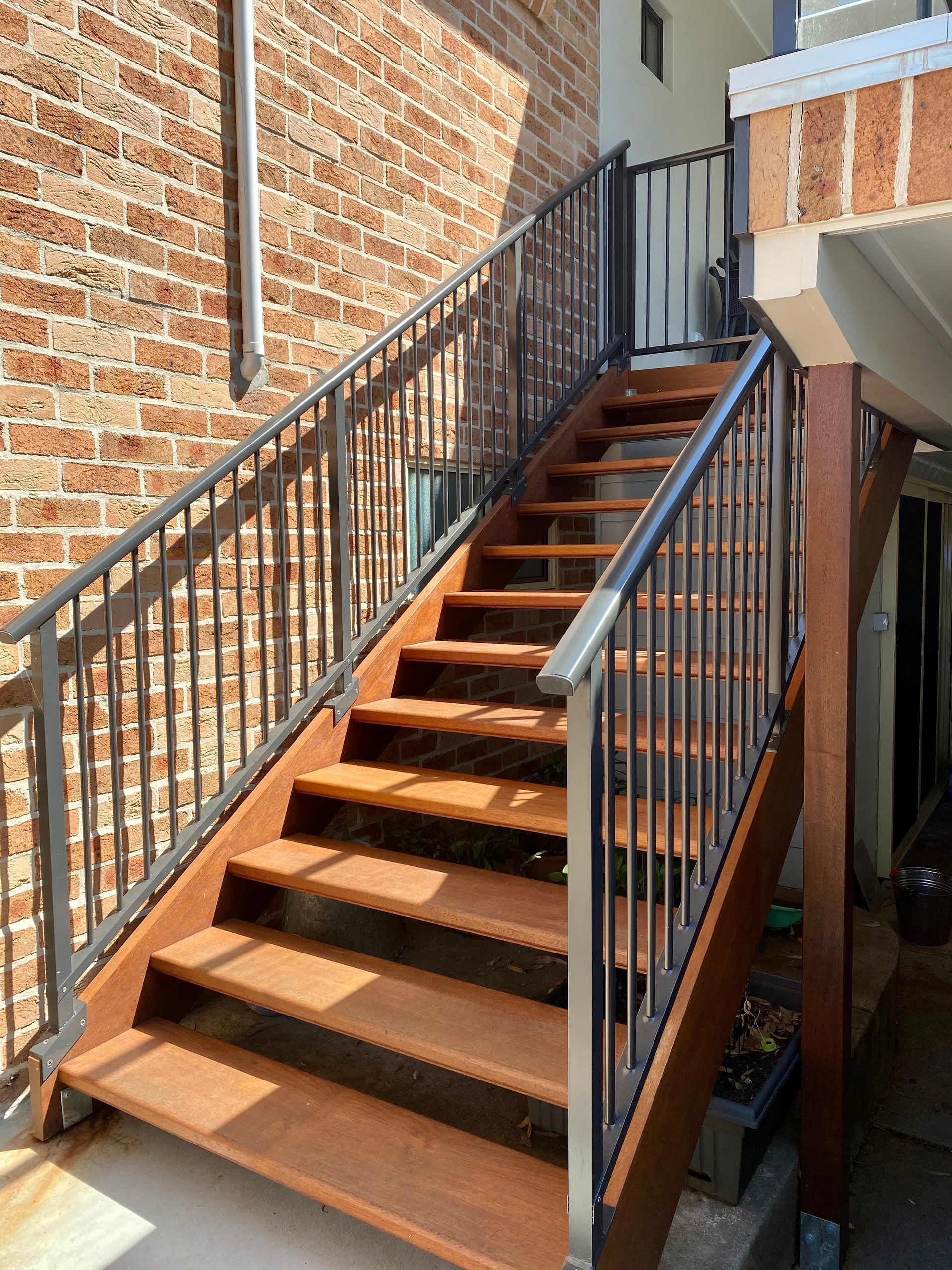 Outdoor metal staircase with handrails, leading to a doorway. Brick wall and wooden supports.