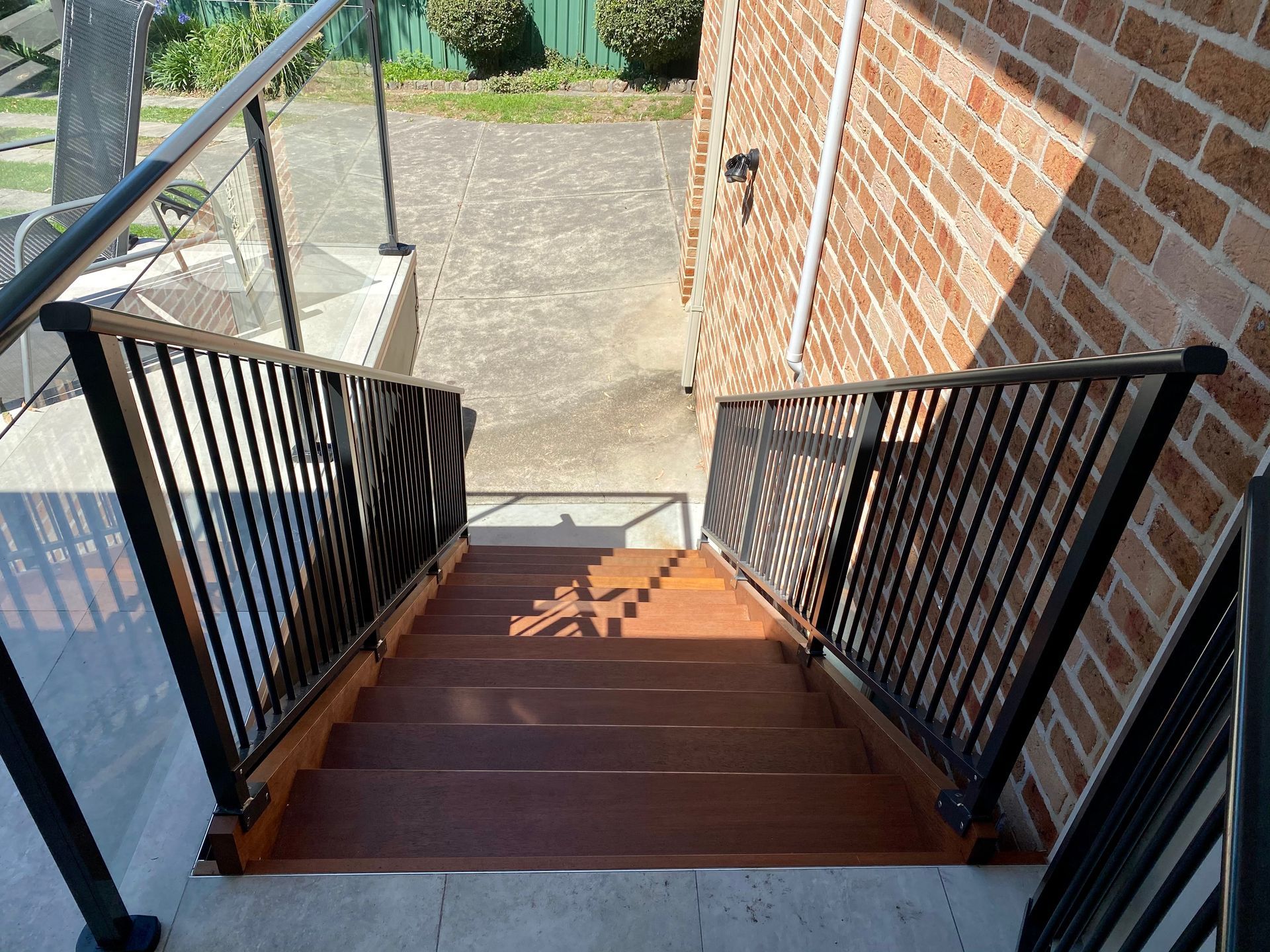 Wooden staircase with black metal railings descending from brick building.