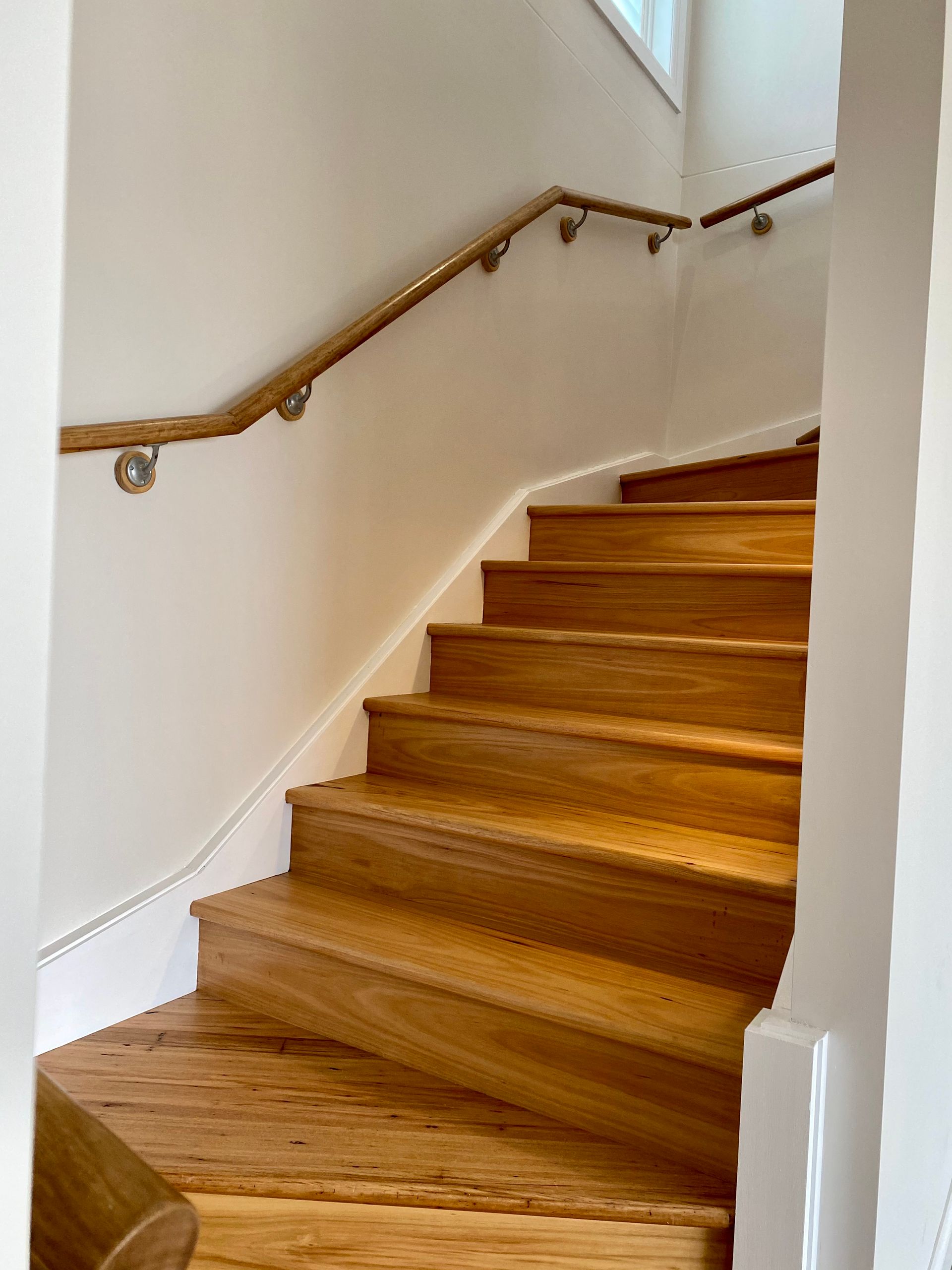 Wooden staircase with a wooden handrail against a white wall.