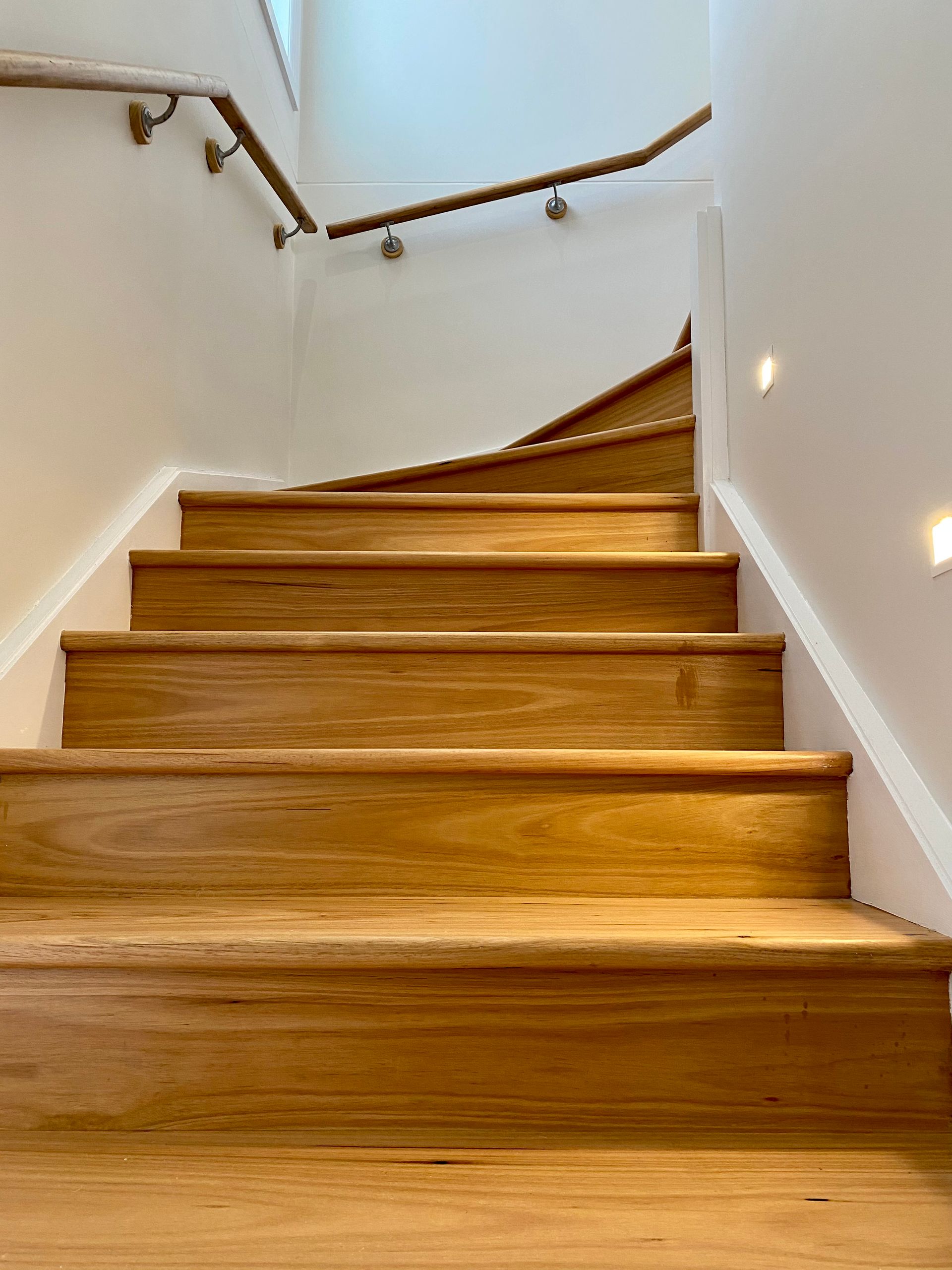 Wooden stairs with a brass handrail, lit by recessed lights, leading upwards.
