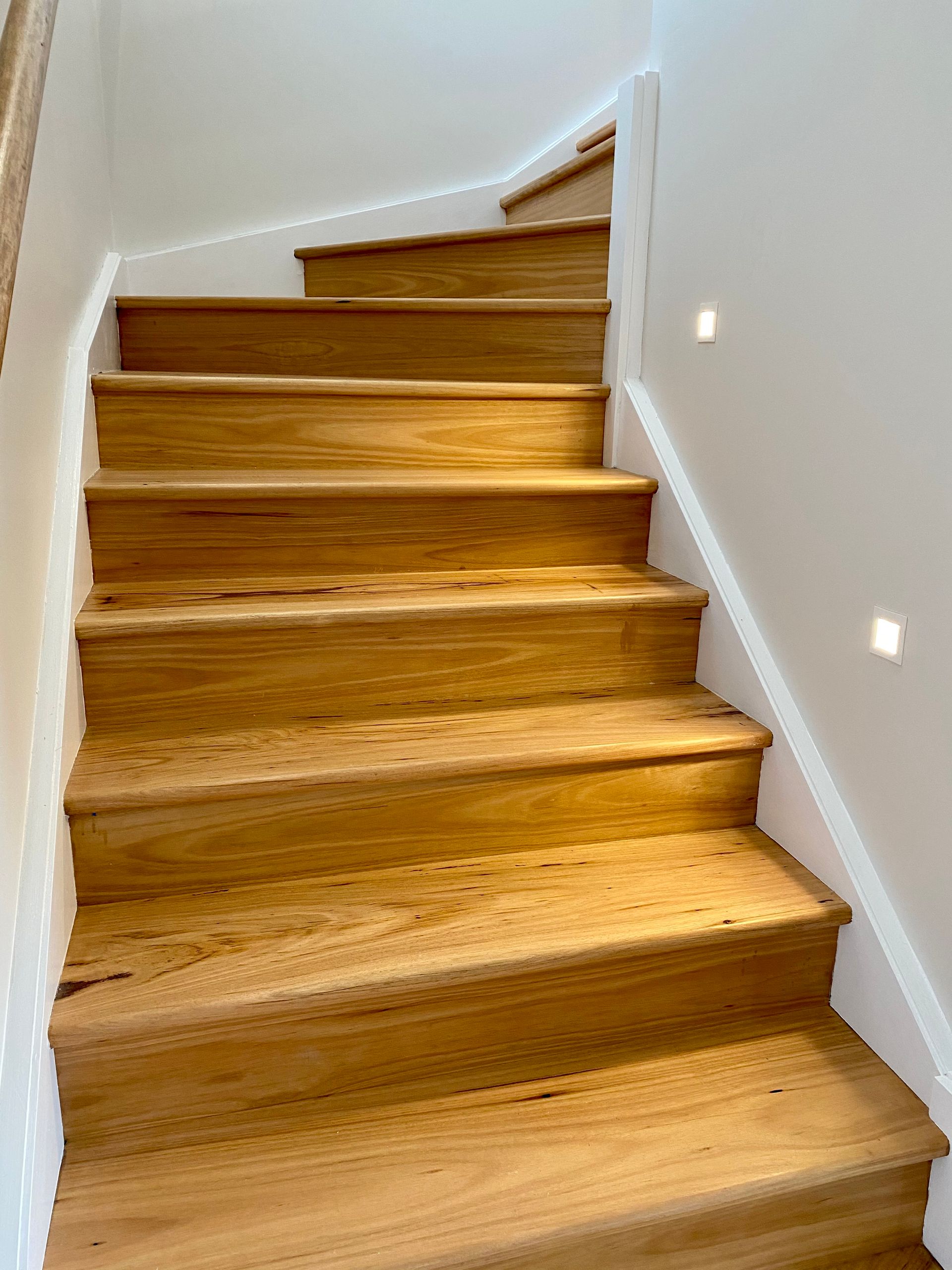 Wooden staircase with white trim, lit from above and with embedded lights in the wall.