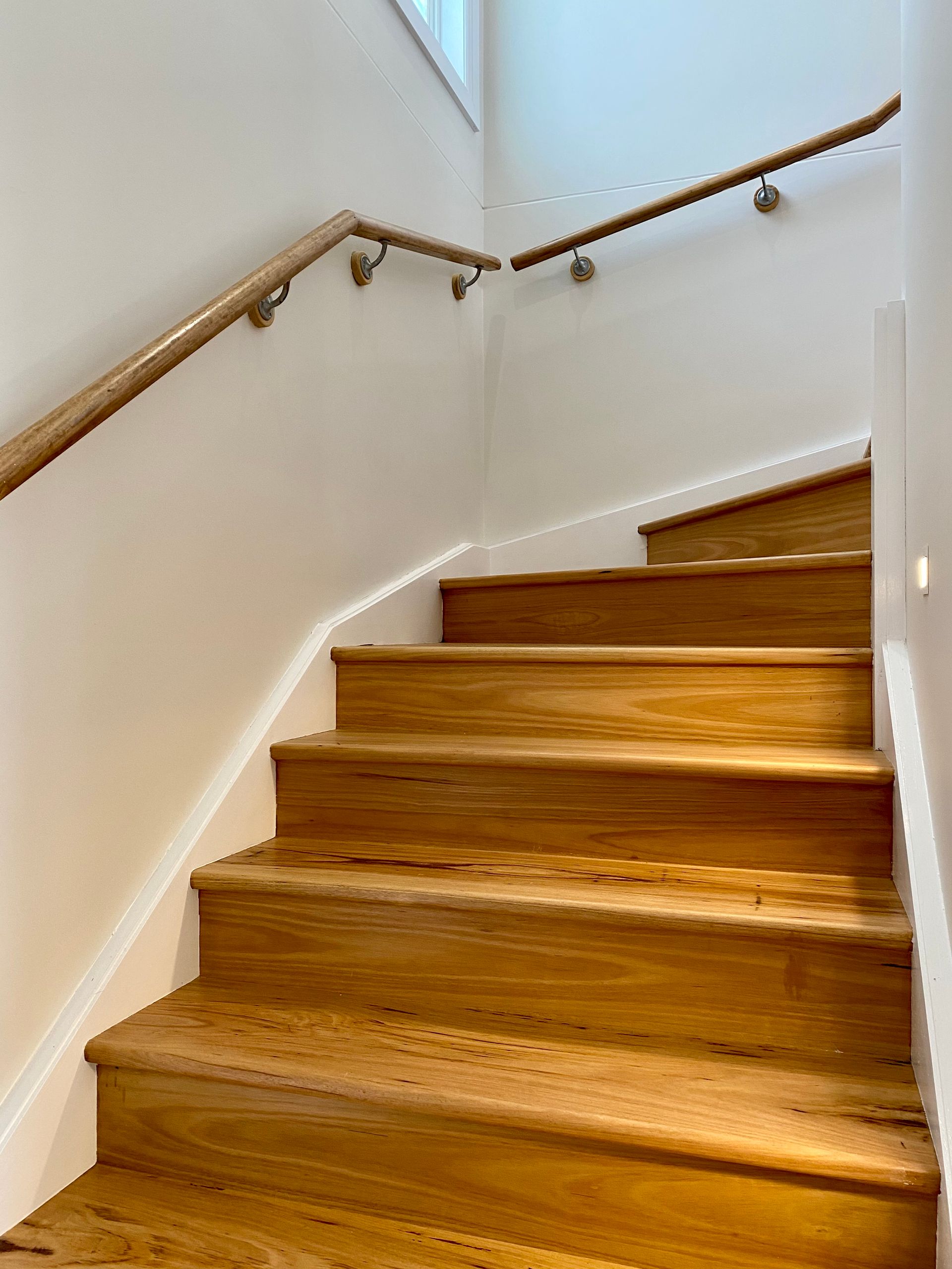 Wooden stairs with a handrail against a white wall.