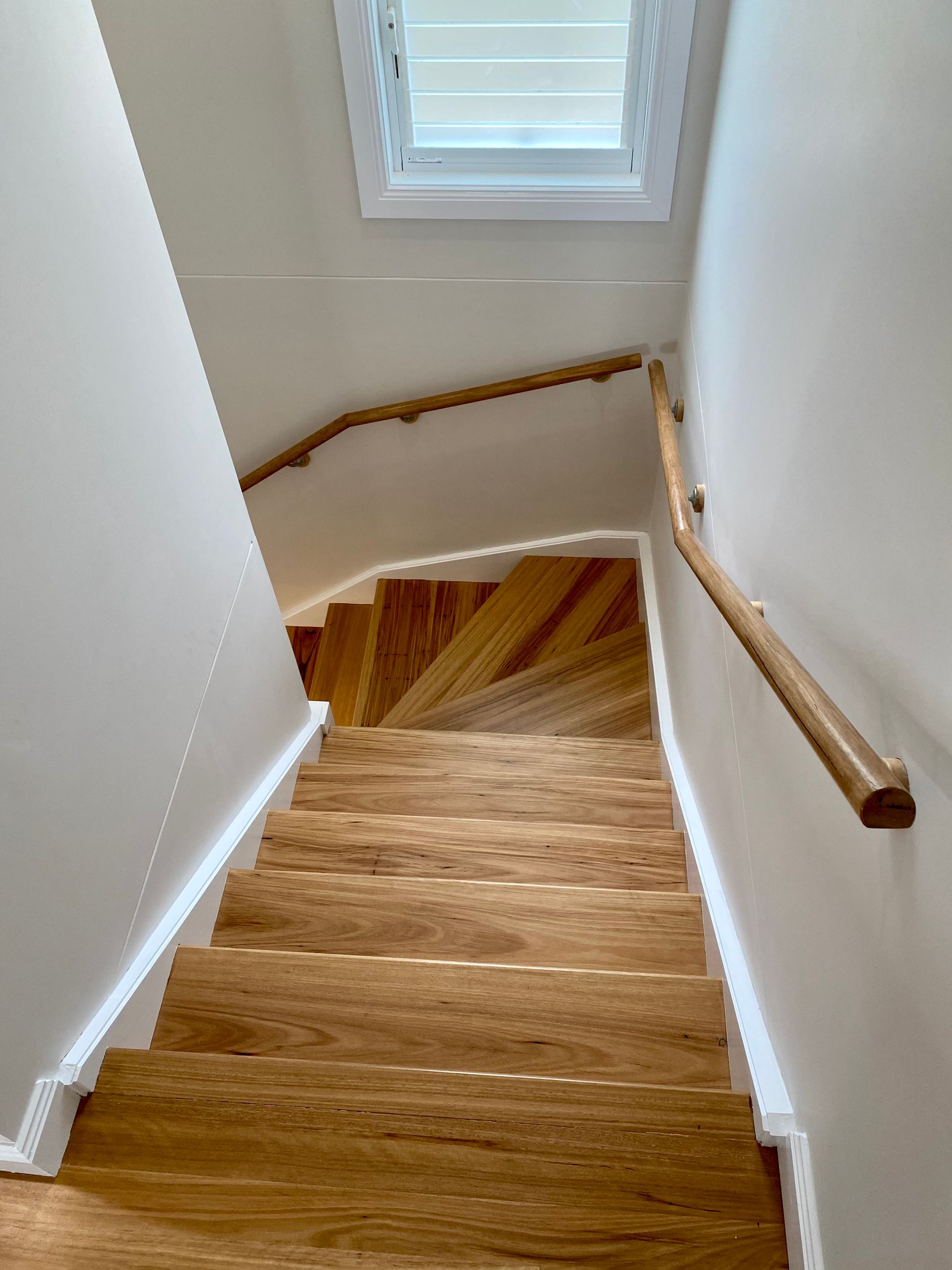 Wooden staircase with light-colored steps, two wooden handrails, and a small window at the top.