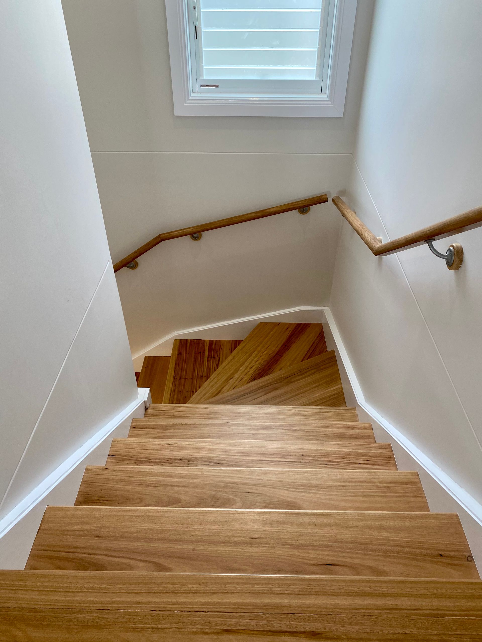Wooden staircase with handrails, ascending from bottom to top, lit by a small window.
