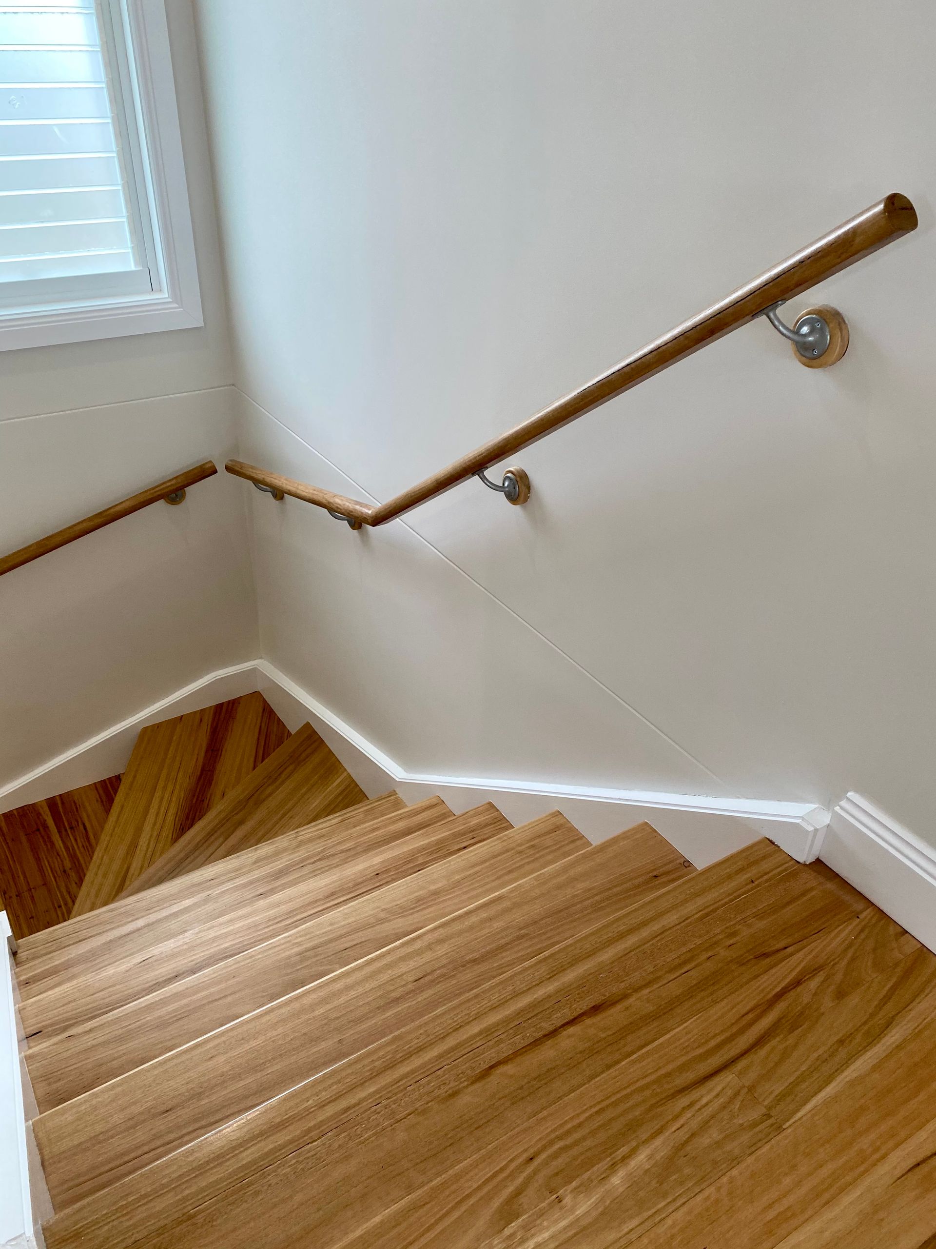 Wooden staircase with a wooden handrail along a white wall.