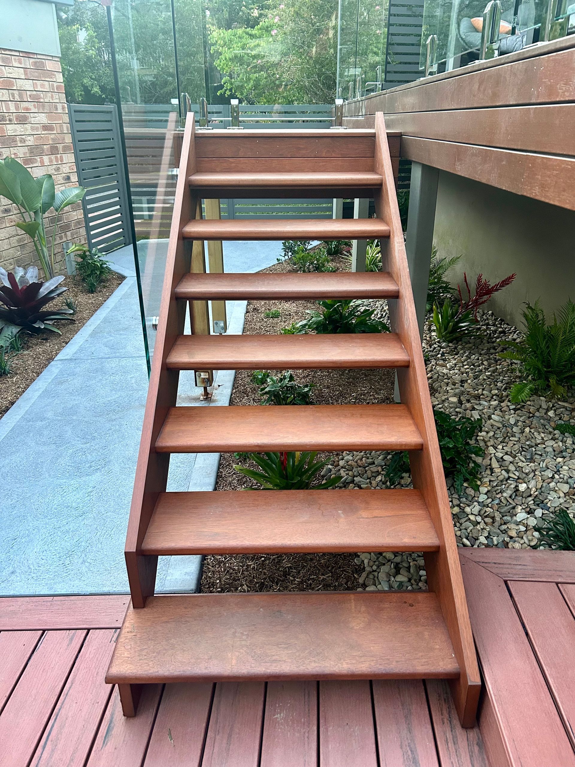 Wooden outdoor stairs leading to a deck, surrounded by landscaping.