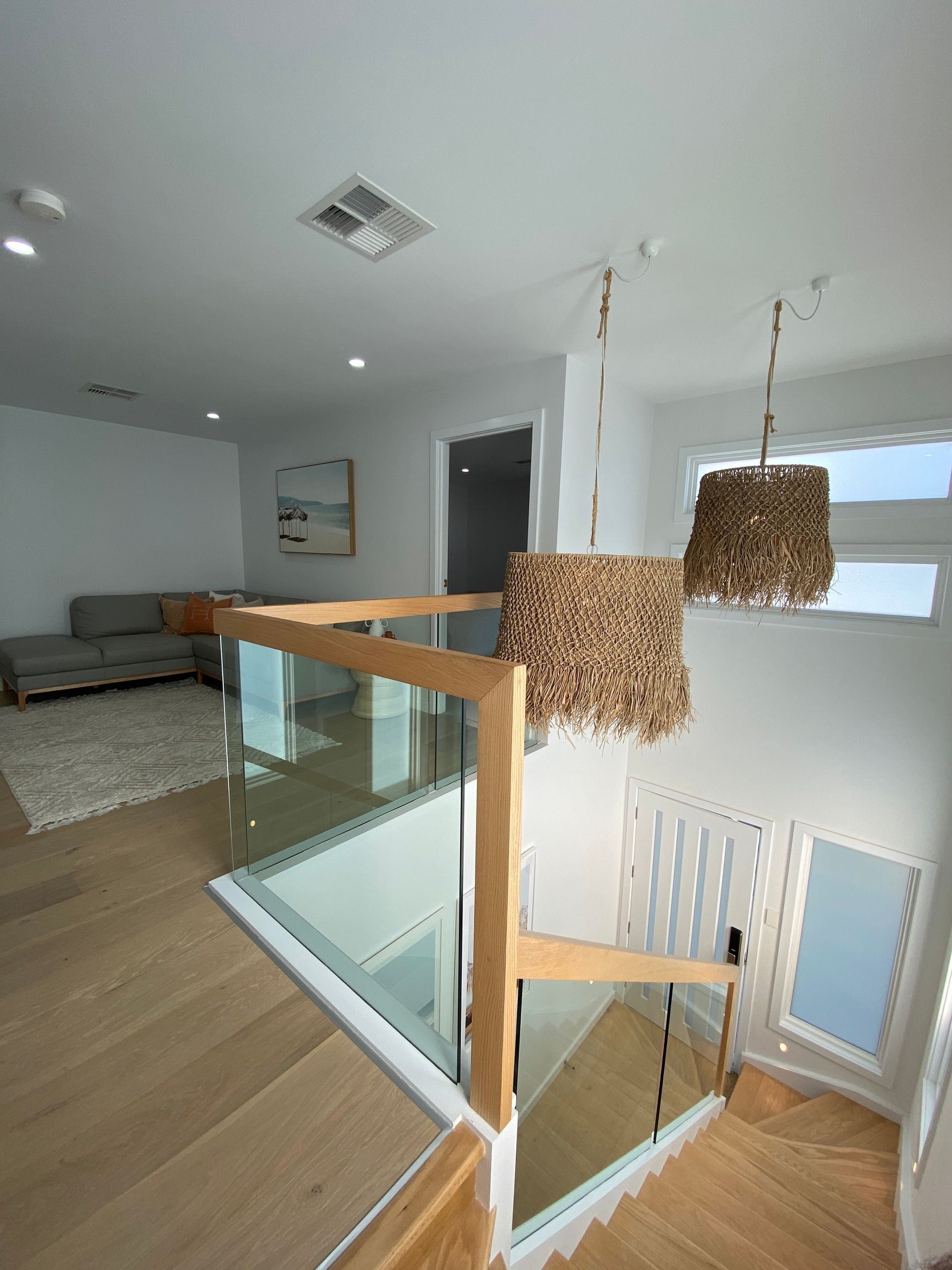 Wooden staircase with glass railing, leading to an open kitchen and dining area.