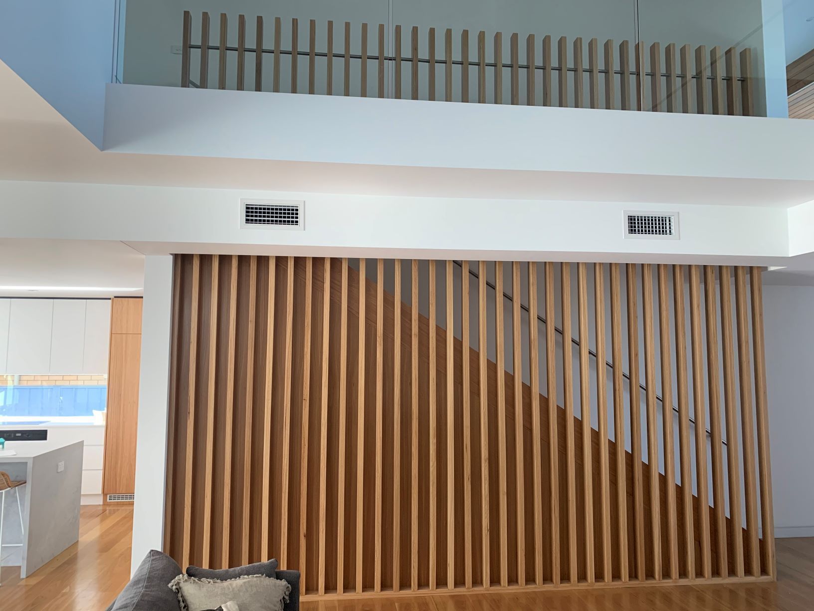 Wooden slat wall with staircase and second-floor railing. Open plan interior with white walls, natural wood tones.