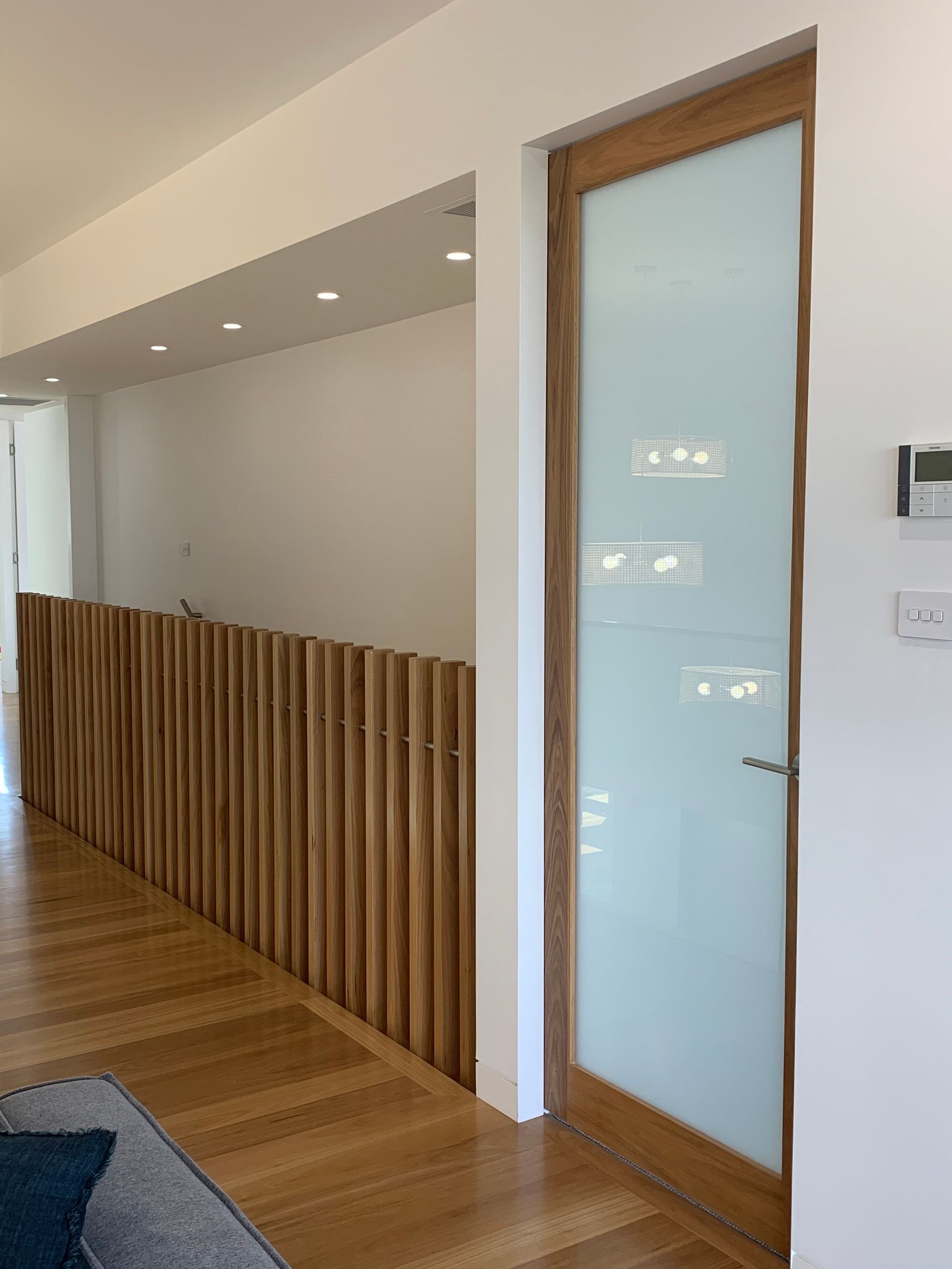 Wooden door with frosted glass, next to a wood slat railing, and hardwood floors.