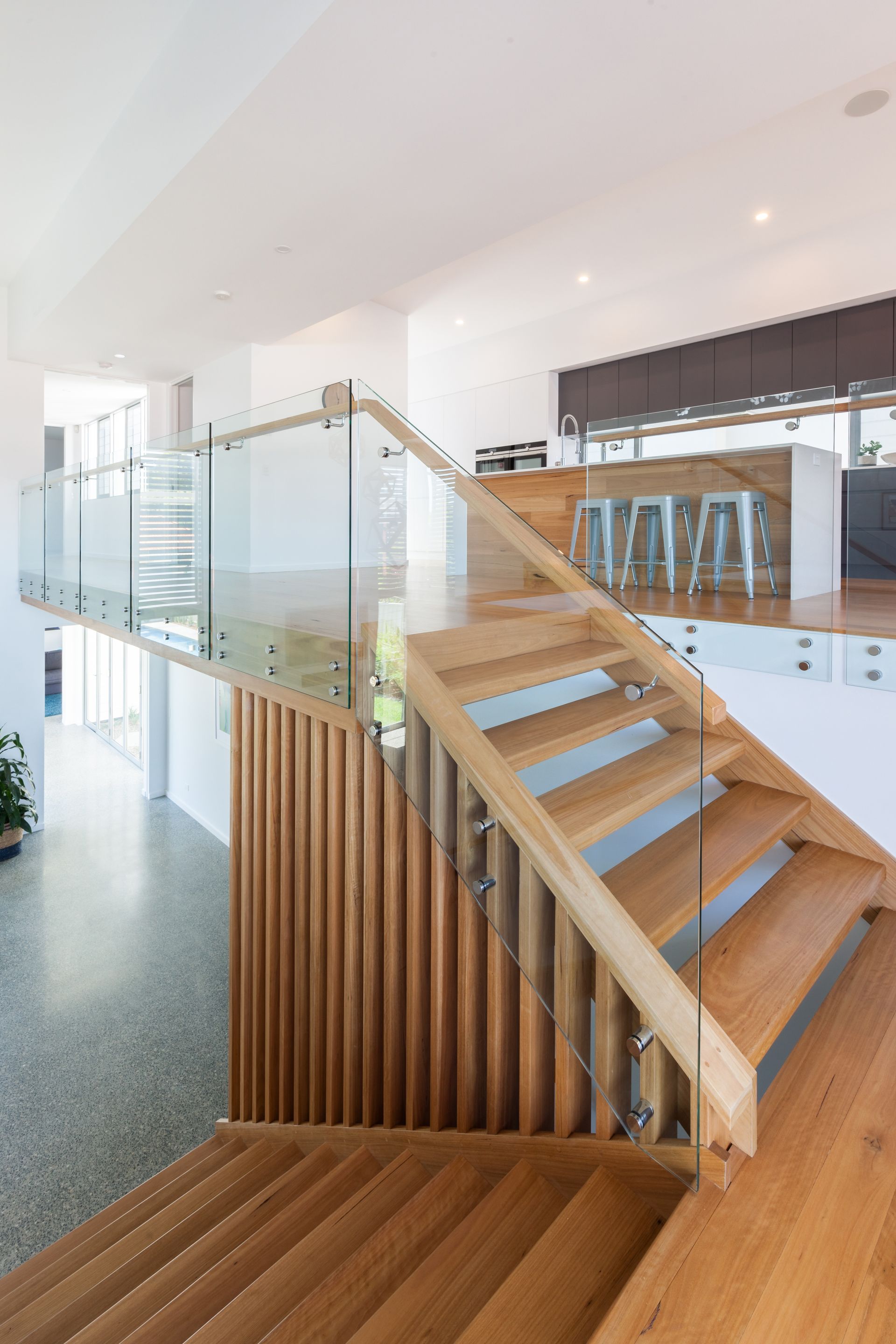 Wooden staircase with glass railing in a modern, bright home; view from above.