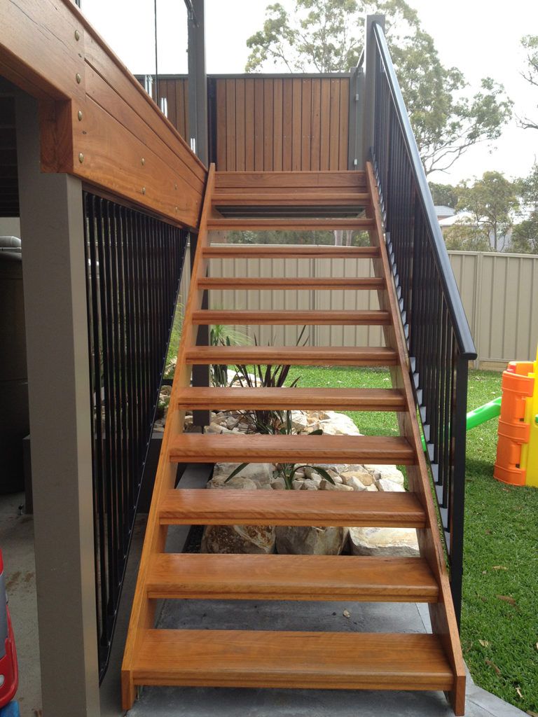 Wooden outdoor staircase with black metal railing, leading up to a deck.