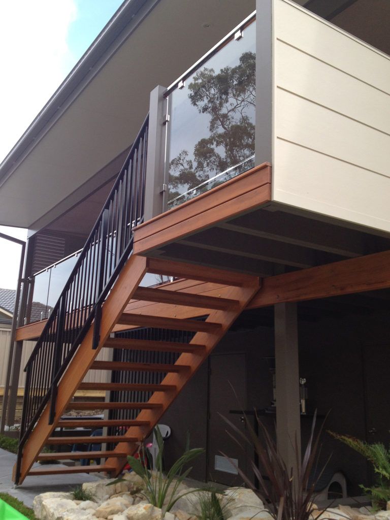 Wooden outdoor staircase leading to a deck with a glass railing, under a house's awning.