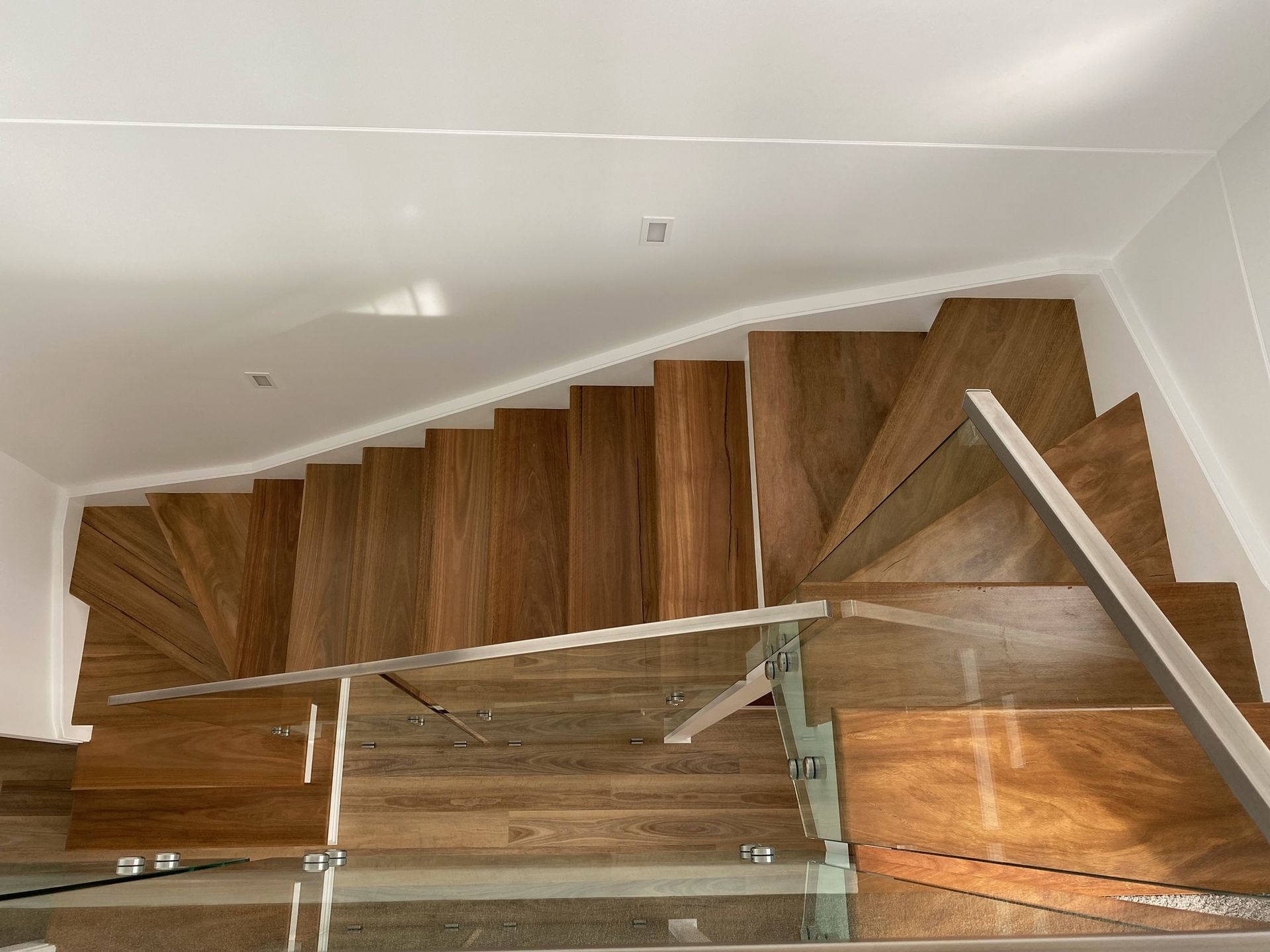 Wooden staircase with glass railing and white walls.