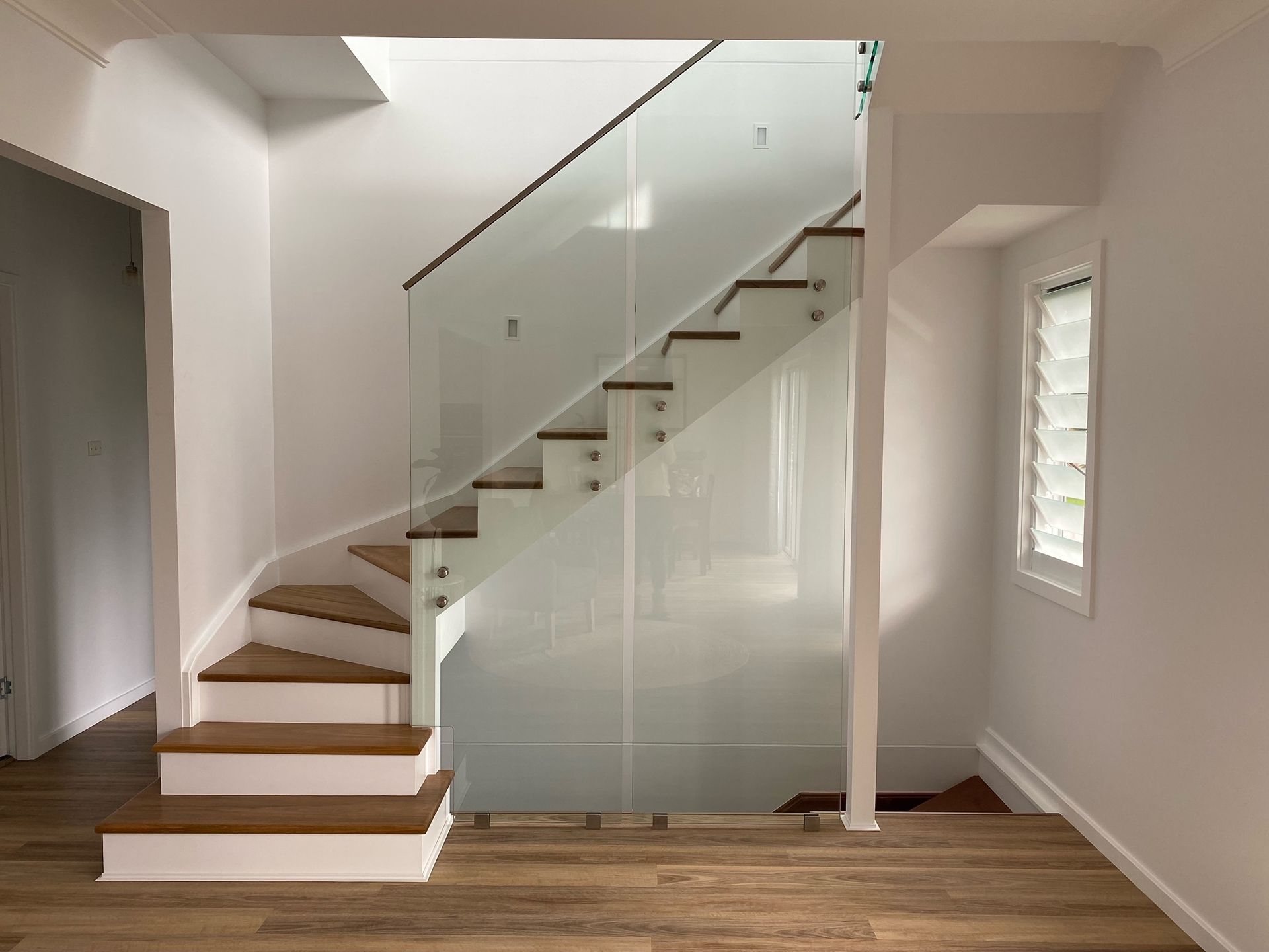 Staircase with wood steps, glass railing, and white walls.