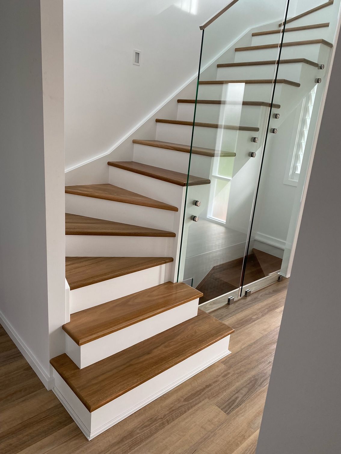 Wooden staircase with glass railing, white risers, and wood flooring.