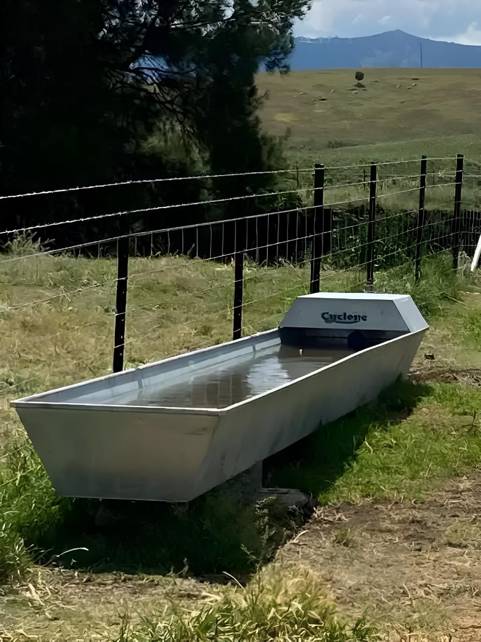 A Large Metal Water Trough is Sitting in the Grass Next to a Fence — MacCallum & Company In Scone, NSW