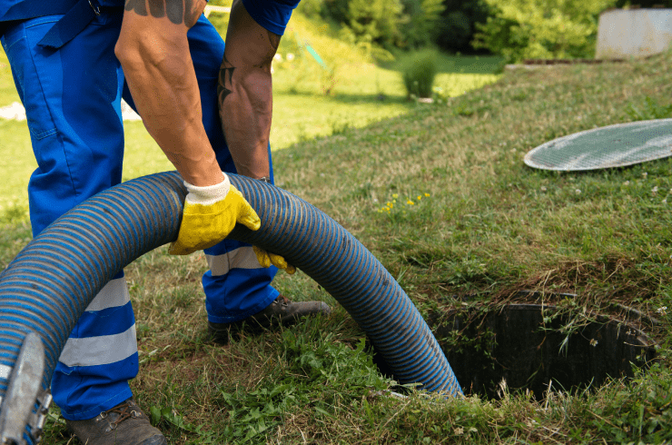 Man in blue overalls and gloves, holding a hose to pump a septic tank.