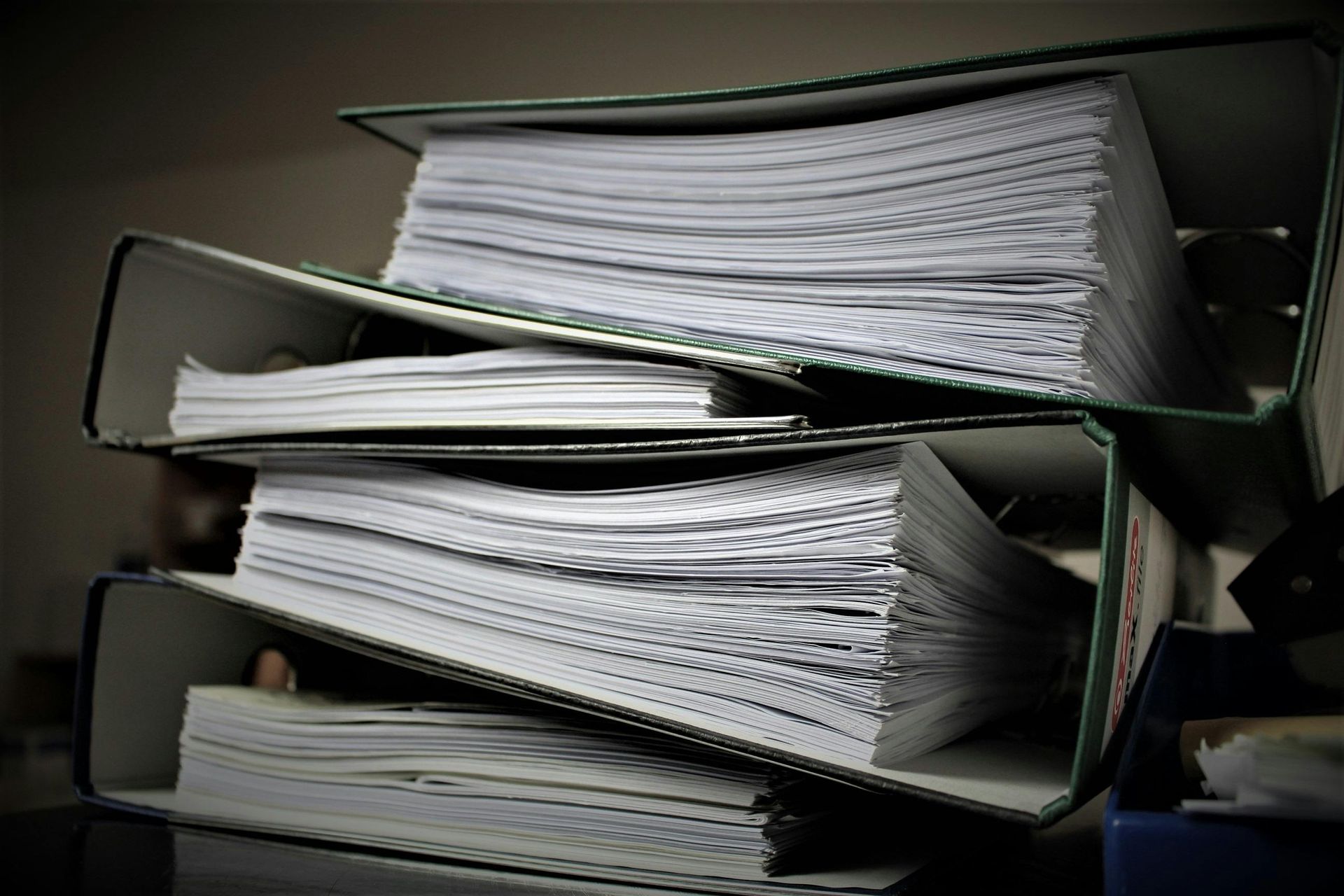 A stack of three green office binders filled with white paper documents.