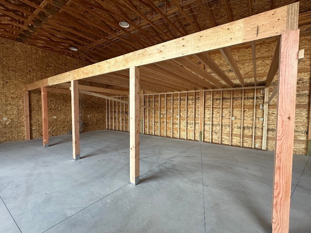 Interior of a building under construction, wooden framework, concrete floor, unfinished walls, overhead beams.