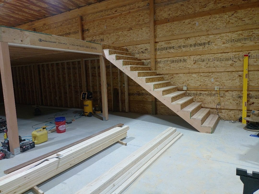 Interior view of a wooden staircase under construction. The stairs lead upwards within a partially constructed building.