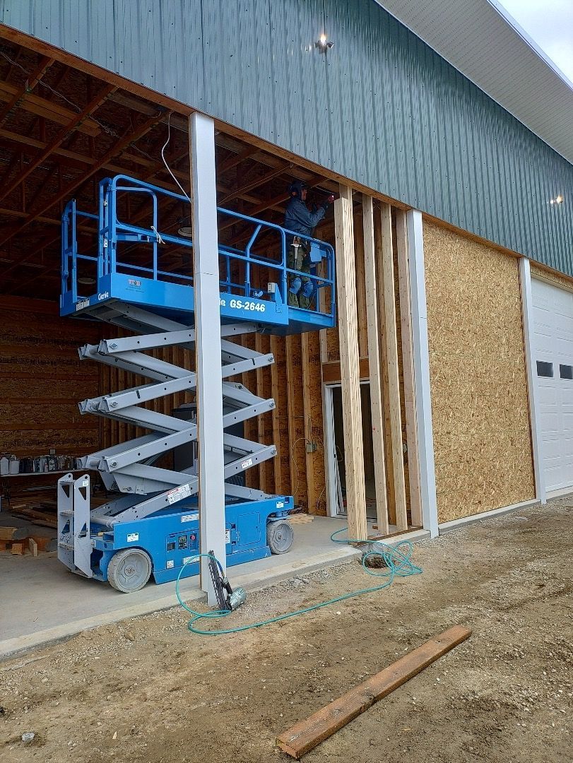 Construction worker on a blue scissor lift installing siding on a building's exterior wall.