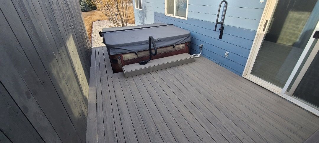 Hot tub on a wooden deck next to a blue wall and a sliding glass door.