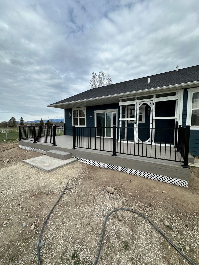 Blue house with black railing deck, gravel yard, and cloudy sky.