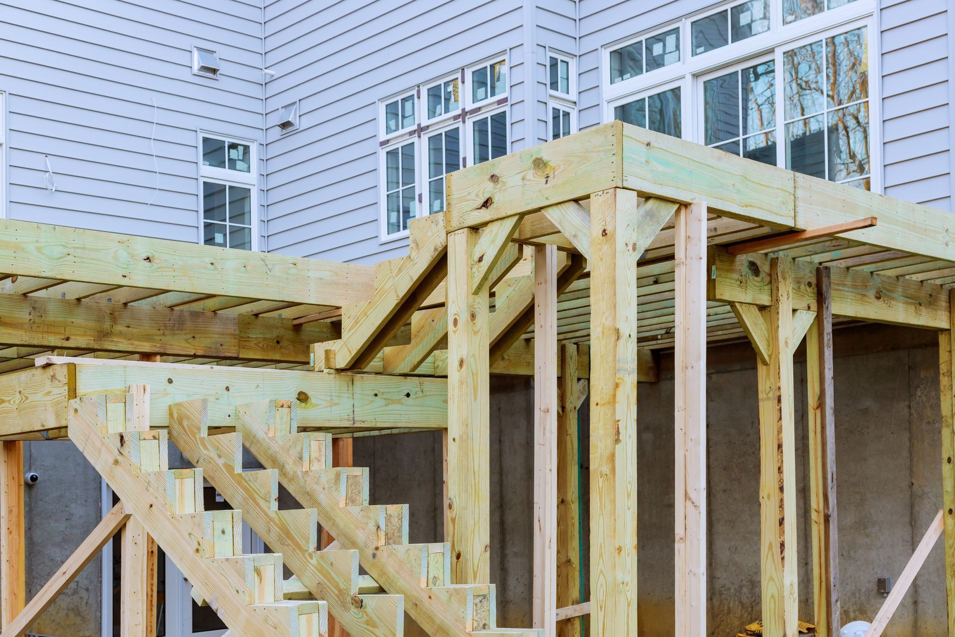 Wooden deck and stairs under construction, attached to a light gray building with windows.