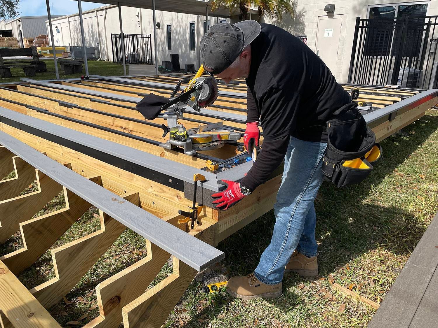 A person wearing work gloves using a clamp on deck construction outside.