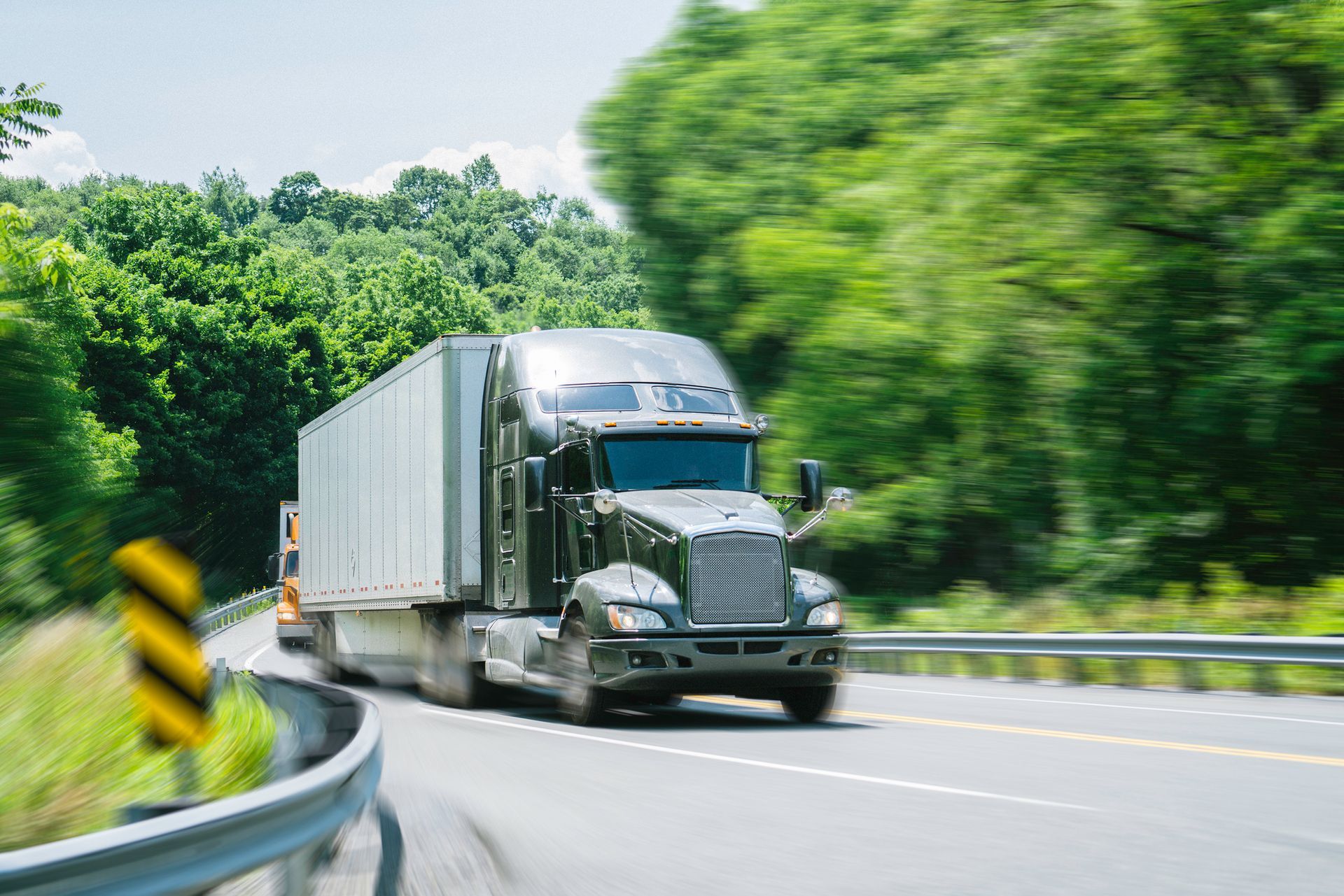 A semi truck is driving down a highway next to trees.