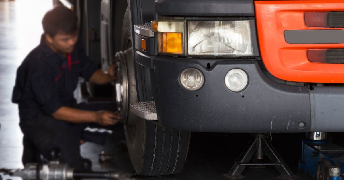 The front of a black and orange trailer truck with a worker kneeling down to inspect one of the fron