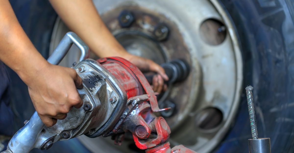 A focus shot of a worker's hands using a pneumatic gun to adjust the lug nuts of a truck tire wheel.