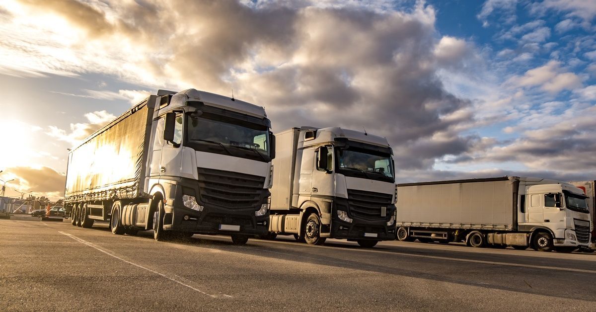 A low-angle shot of three fleet trucks in a parking lot. The setting sun peaks through the clouds.