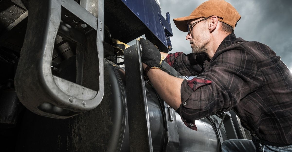 A man in glasses, a cap, a flannel shirt, and black gloves, working on trailer components.