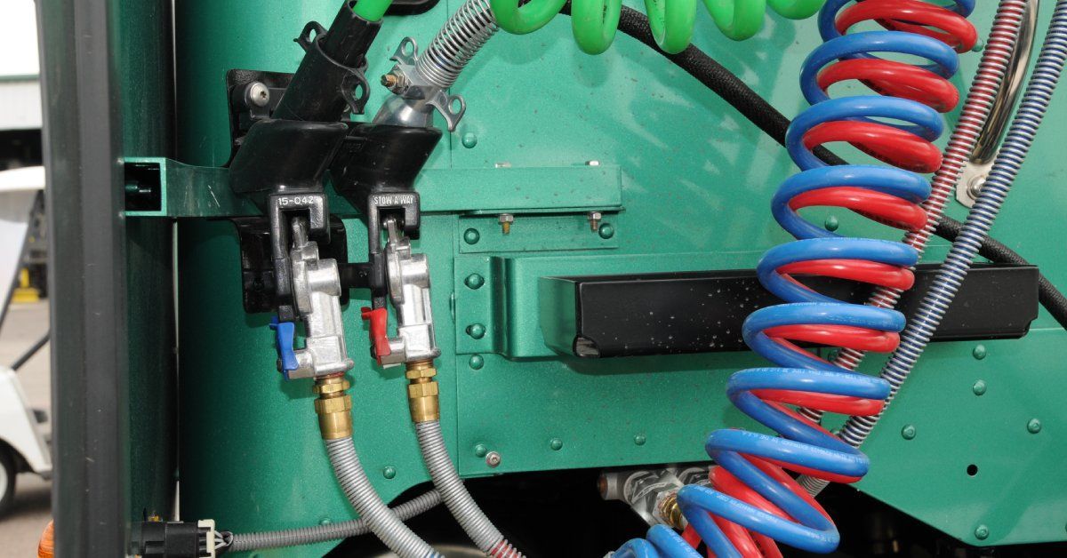 Three coil-shaped air hoses attached to the back of a semitruck's cab. The hoses are green, red, and blue.