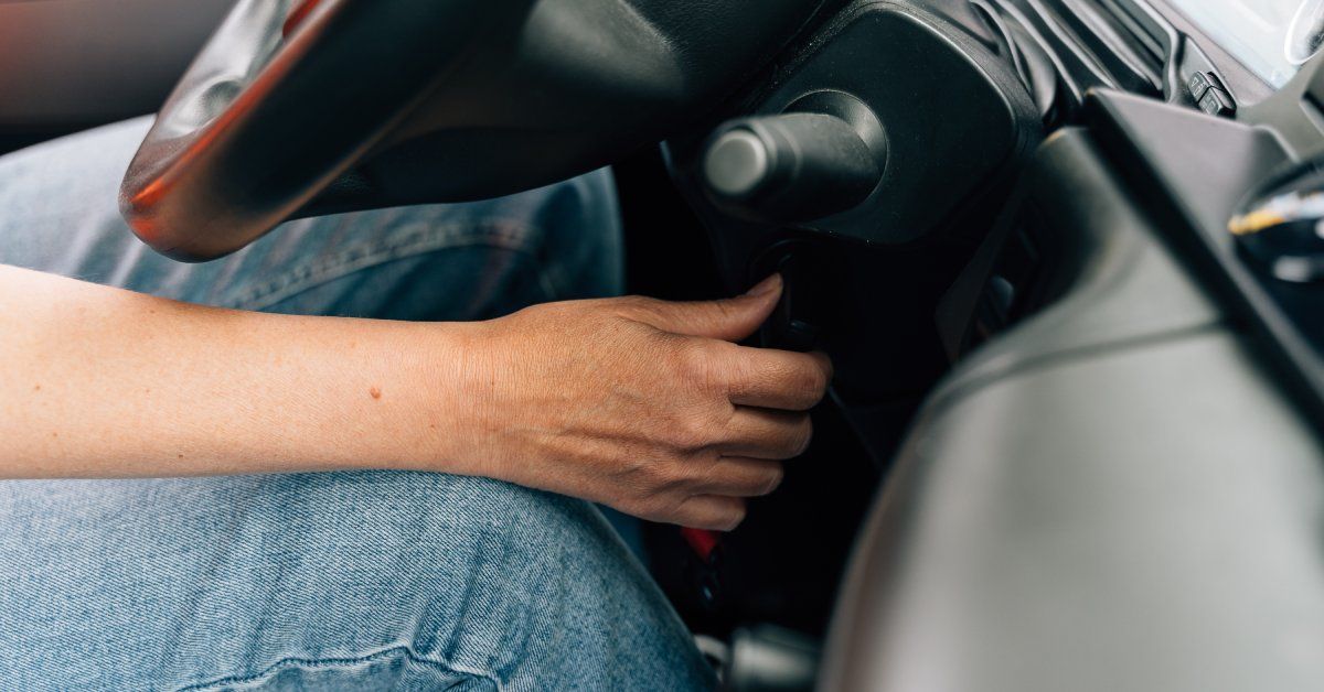 A close-up of a trucker in jeans reaching a hand forward to start the ignition of their semi.