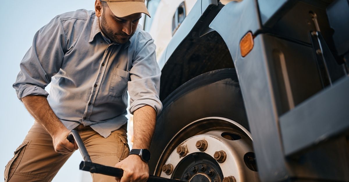 A man using a lug wrench to remove the lugs from one of the tires on a black and white semitruck.