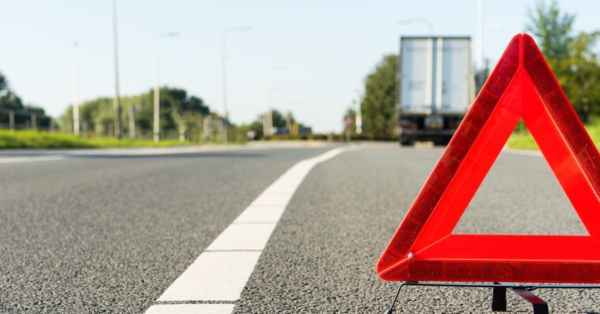 An orange warning triangle set up on the shoulder of a highway, a broken-down semitruck a bit ahead