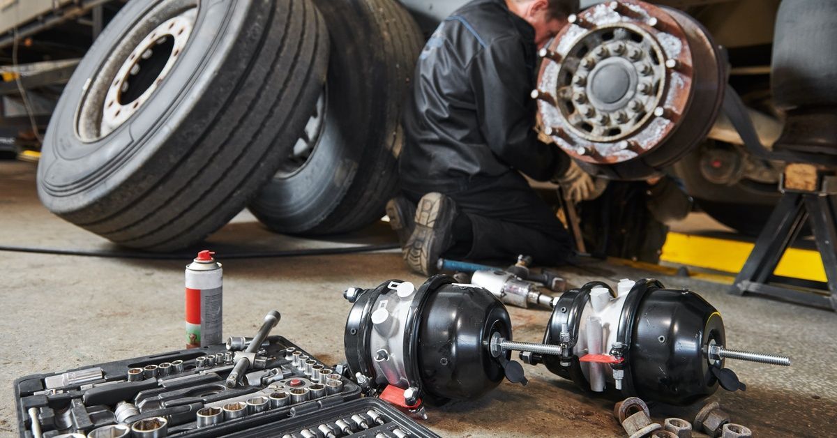 A man working on the tire and brake system of a semitruck. On the ground is a toolbox and parts.