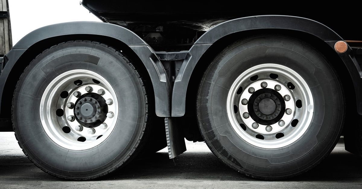 A close-up of two wheels on a semitruck on asphalt. The hubs are shiny silver, and the wheels are black rubber.