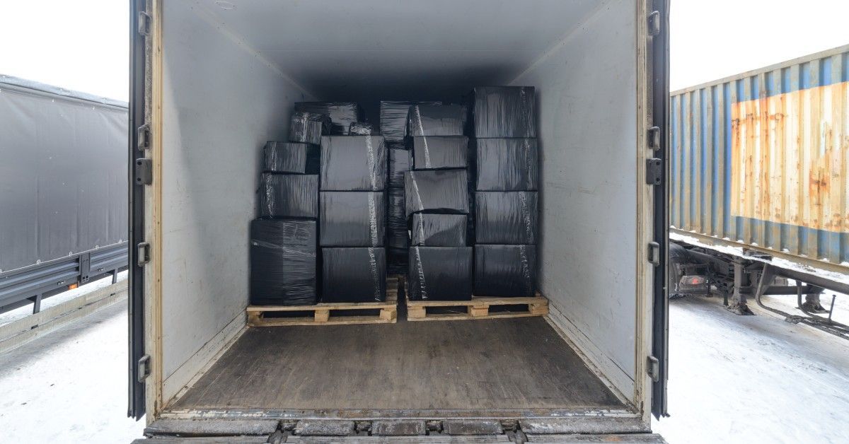 The inside of a freight trailer loaded up with boxes wrapped in black plastic and sitting on top of pallets.