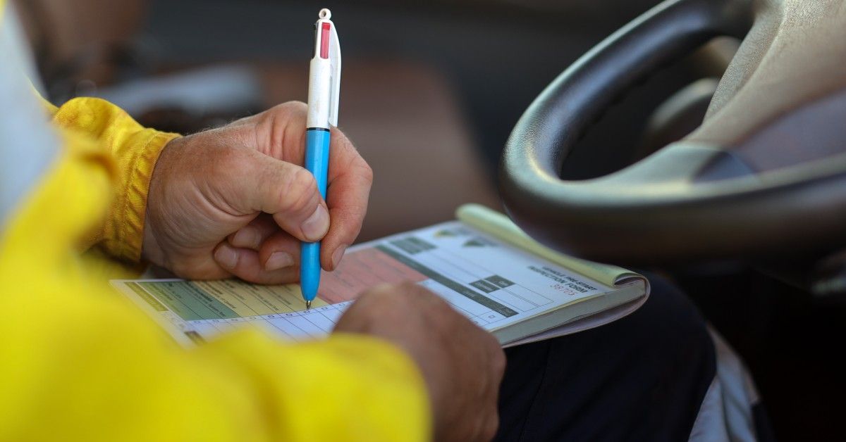 A close-up of a trucker sitting in his semitrailer's cab and using a pen to write an inspection.