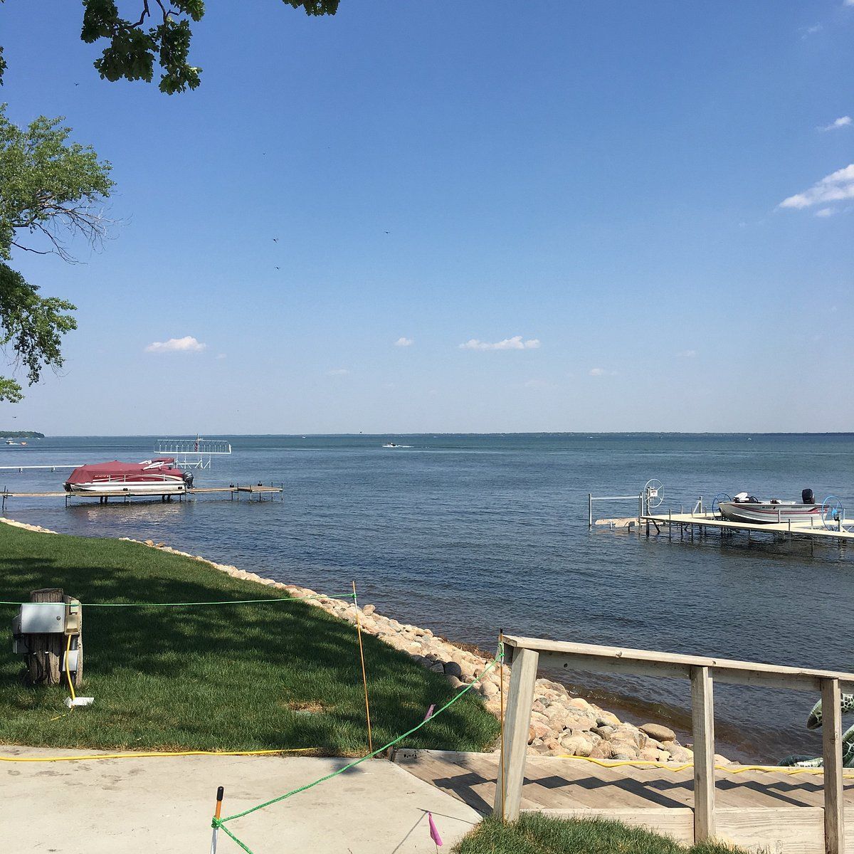 Sunny lakeside with two small boats at a dock, rocky shoreline, and clear blue water under a bright sky