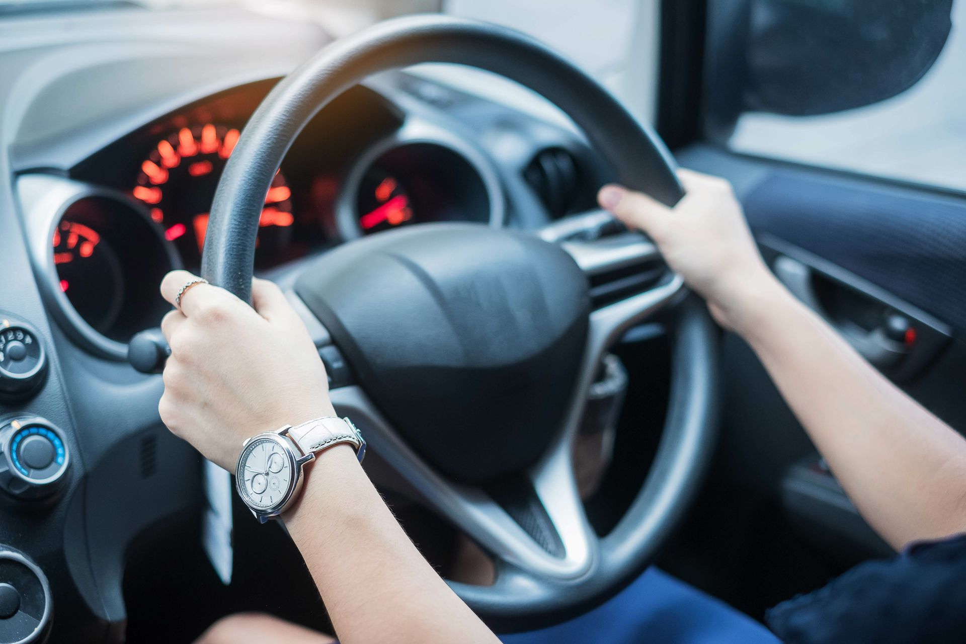 Person’s hands holding a black steering wheel, driving inside a car. A watch is on their left wrist.