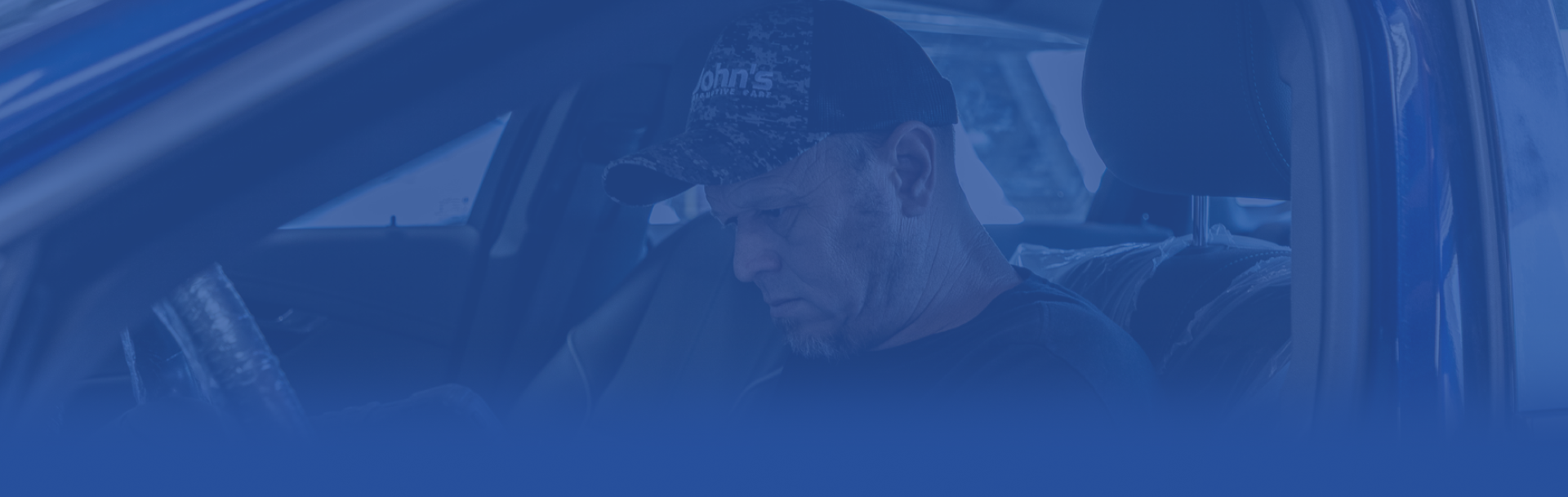 Man in a car, looking down. Dark setting, blue tone.