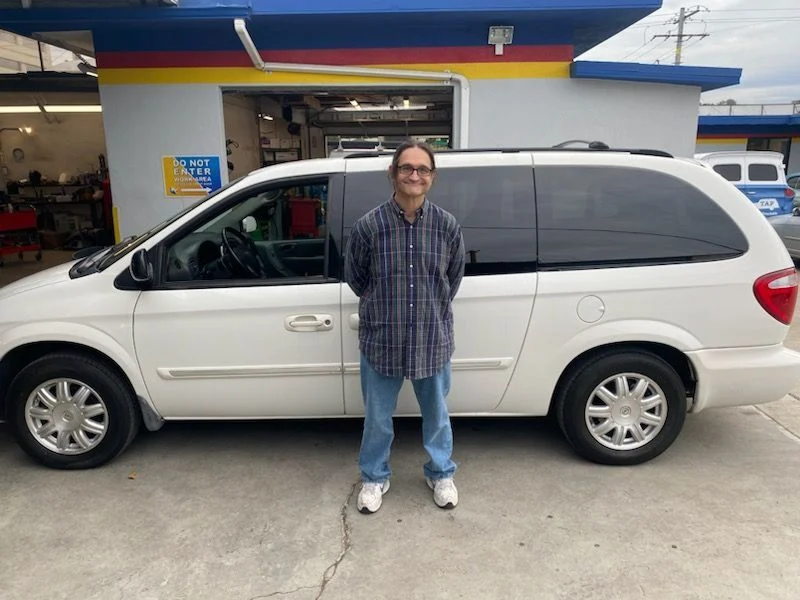 Man standing beside a white minivan in front of a garage.