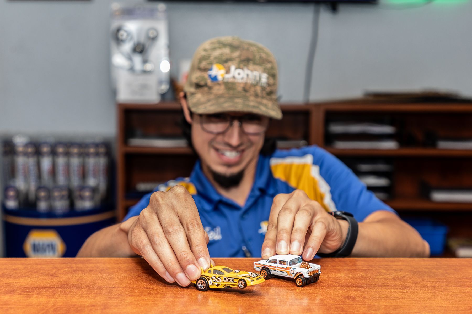 Man in uniform smiling, playing with toy cars on a counter in a shop.
